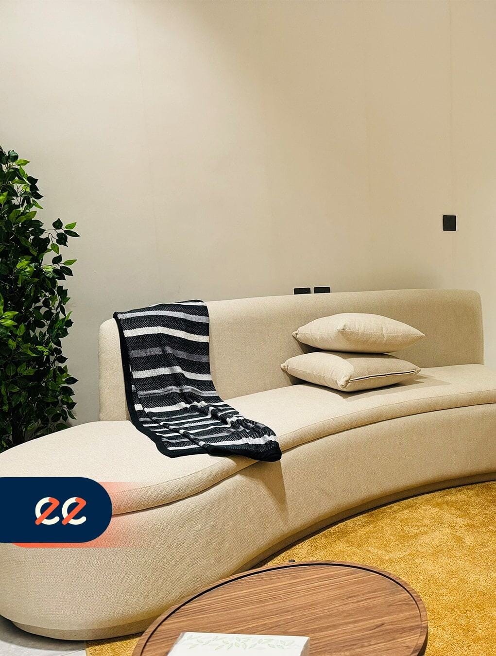 تصوير أريكة بيضاء أنيقة مع وسادتين وغطاء مخطط أسود وأبيض على أحد الأذرع، بجانب نبات أخضر داخلي، مع ديكور حديث لمشاريع إيلفينز.