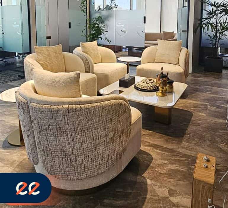 كرسي مريح مع أريكة فاخرة في غرفة انتظار أنيقة ومميزة بألوان دافئة وديكور عصري، مع نافذة واسعة وإضاءة جيدة لخلق جو مريح وعملي للمكتب أو الشركة.