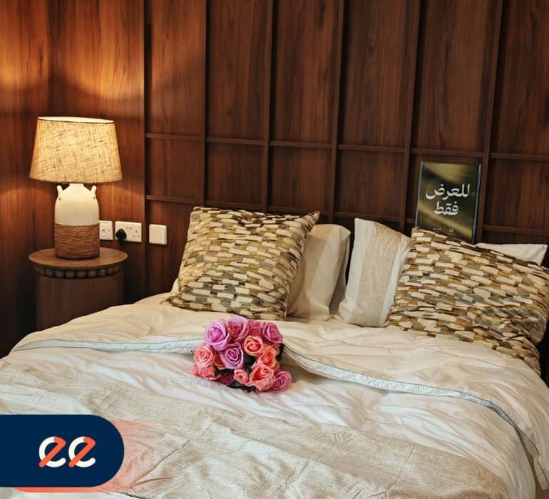 ديكور سرير لغرف الفنادق مع وسائد وورد وسط السرير، إضاءة دافئة وجدارية خشبية، تصميم داخلي أنيق ومريح.