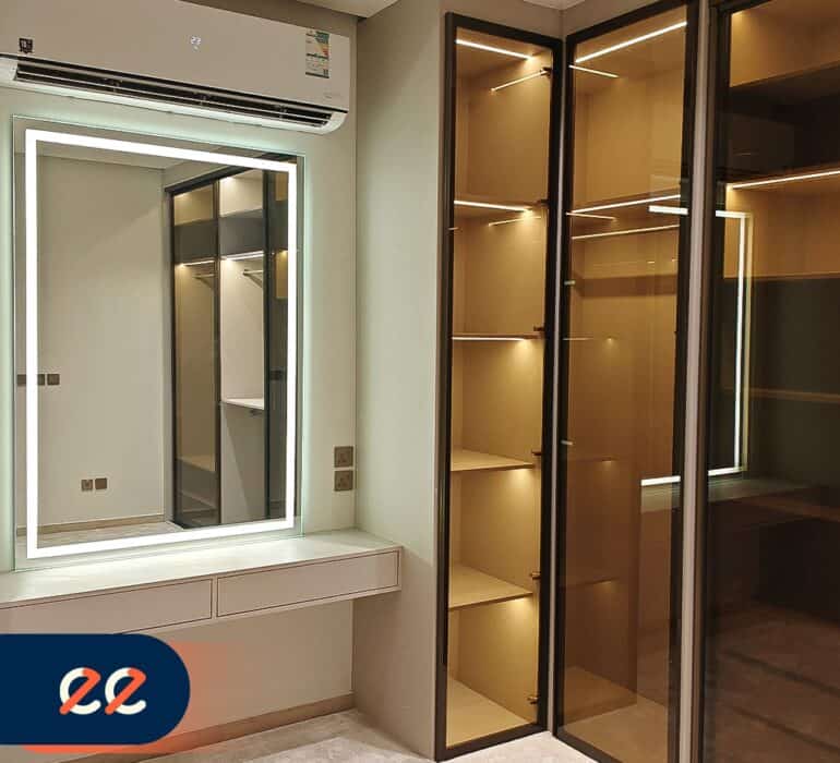 تصريح تصويري يُظهر غرفة مزودة بمرآة ذكية مضاءة ومجموعة خزائن ذات تصاميم حديثة بإضاءة داخلية، مع تكييف هواء وديكور أنيق، يعكس مشاريع إيلفينز في تطوير تصاميم داخلية حديثة ومتقدمة.